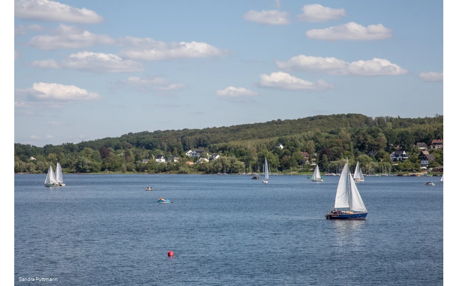Segelboot auf dem ruhigen Möhnesee unter blauem Himmel mit Wolken.