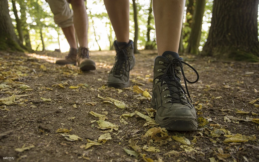 Nahaufnahme von den Beinen zweier Personen in Wanderschuhen auf einem Waldweg.