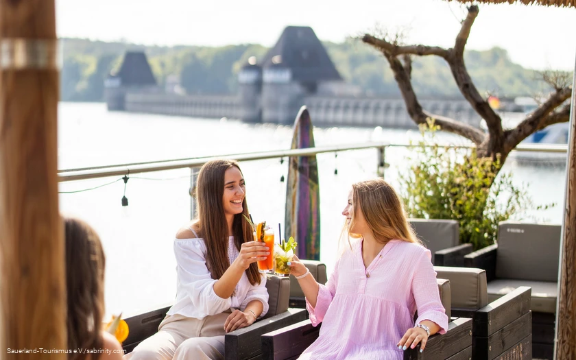 Zwei junge Frauen stoßen mit Cocktails im Restaurant vor der Staumauer an