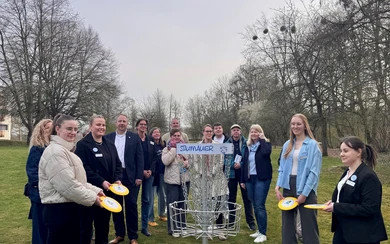 Gruppe von Personen mit Discgolf-Scheiben um einen Discgolf-Korb im Freien