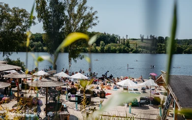 Belebter Strand am Möhnesee mit Sonnenschirmen und Personen, die in der Sonne liegen oder baden.