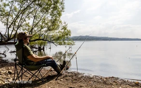 Person sitzt in einem Campingstuhl und angelt am Ufer des Möhnesees.