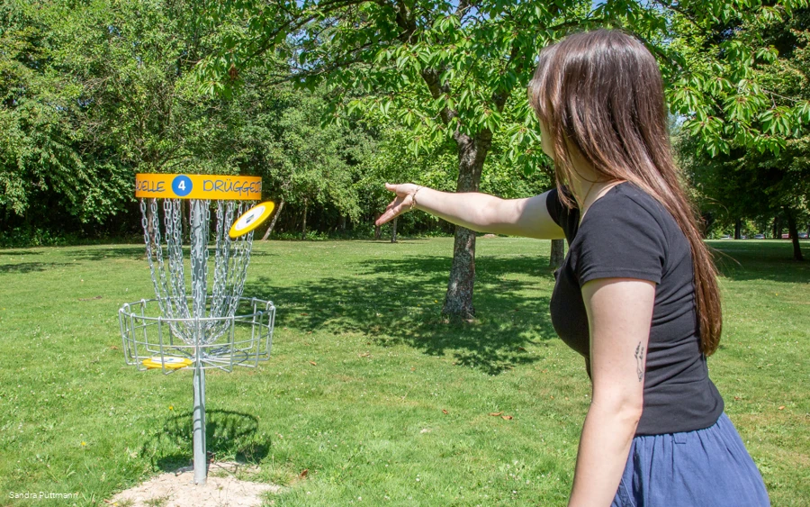 Eiune Person wirf eine Schebe in den Korb des Discgolf Parcours