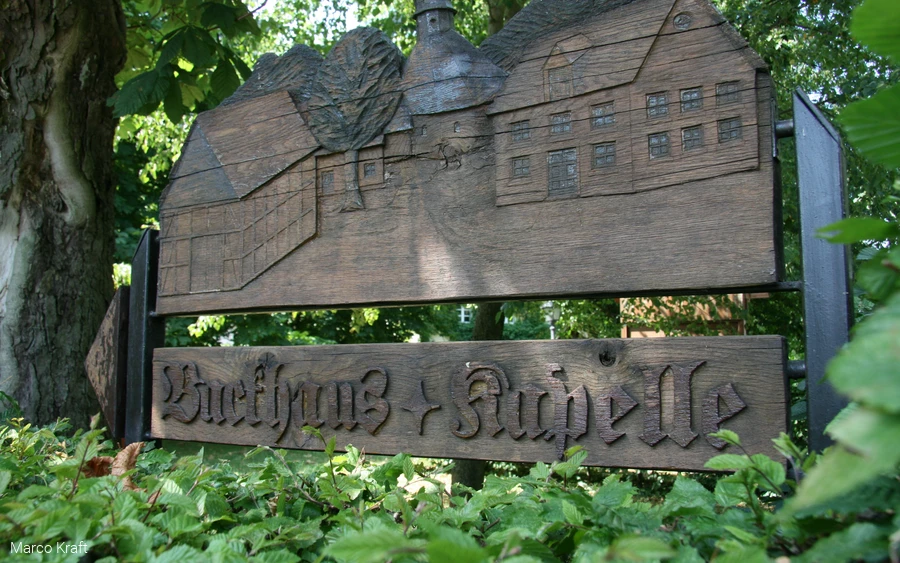 Holzschild mit Reliefdarstellung und Aufschrift „Backhaus + Kapelle"