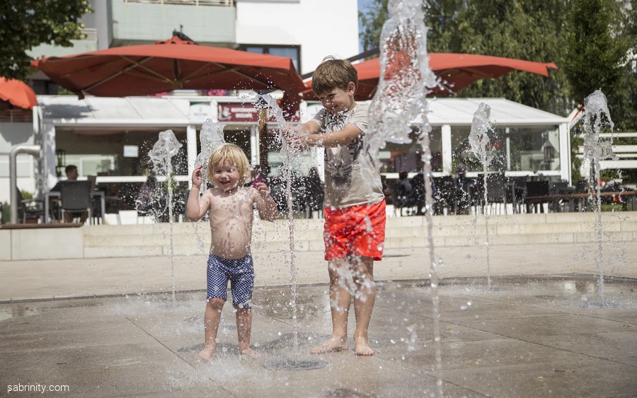 Zwei Kinder spielen in einem Wasserfontänenfeld auf dem Pankratiusplatz in Körbecke.