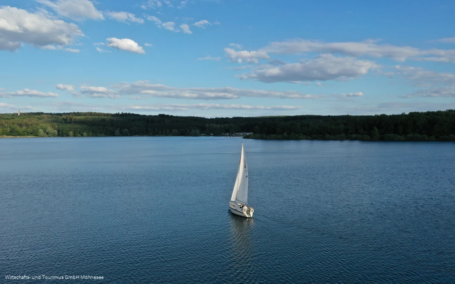 Segelboot auf dem ruhigen Möhnesee unter blauem Himmel mit Wolken.