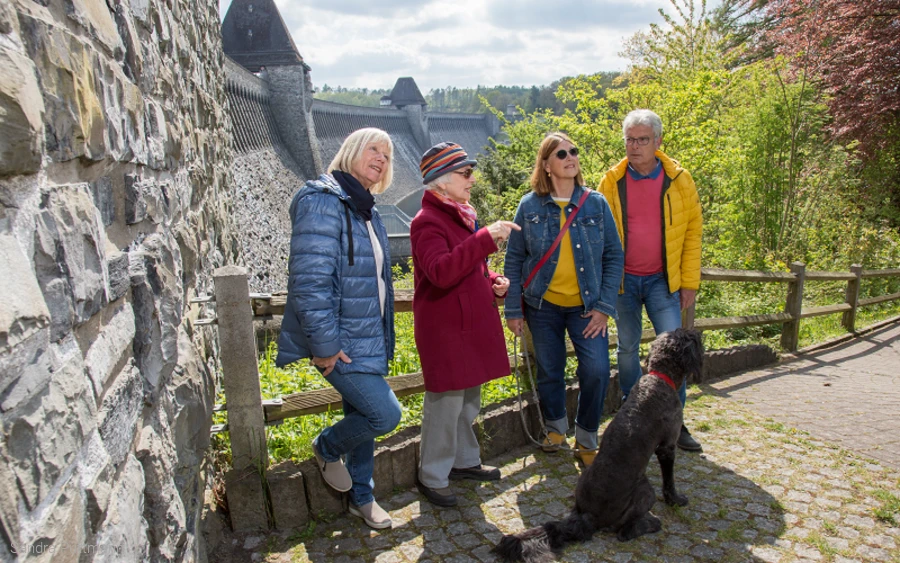 Gruppe von Personen mit Hund steht etwas unterhalb an der Staumauer.