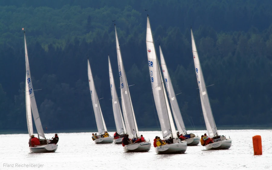 Mehrere Segelboote auf dem Möhnesee vor bewaldeten Hügeln.